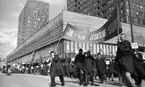 Första maj demonstration 2 maj 1967

Ett första-majtåg går genom centrala Örebro vid varuhuset Krämaren. I förgrunden syns två män klädda i rockar och som bär på en stor banderoll med texten: 