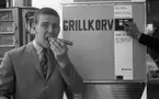 Korvätandet 30 augusti 1968

En man äter en grillkorv som han precis har köpt i en automat. Han är klädd i ljus kavaj, ljus skjorta och mönstrad slips.