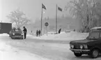 Ånnaboda 12 februari 1968

Bilar och människor befinner sig vid en parkering utanför en byggnad på vintern i Ånnaboda. Det ligger snö på marken. Två bilar står i kö efter varandra och vid den främre bilen står en äldre herre som troligtvis är en parkeringsvakt. Han har en liten biljettmaskin hängande med i rem på sin vänstersida på kroppen.