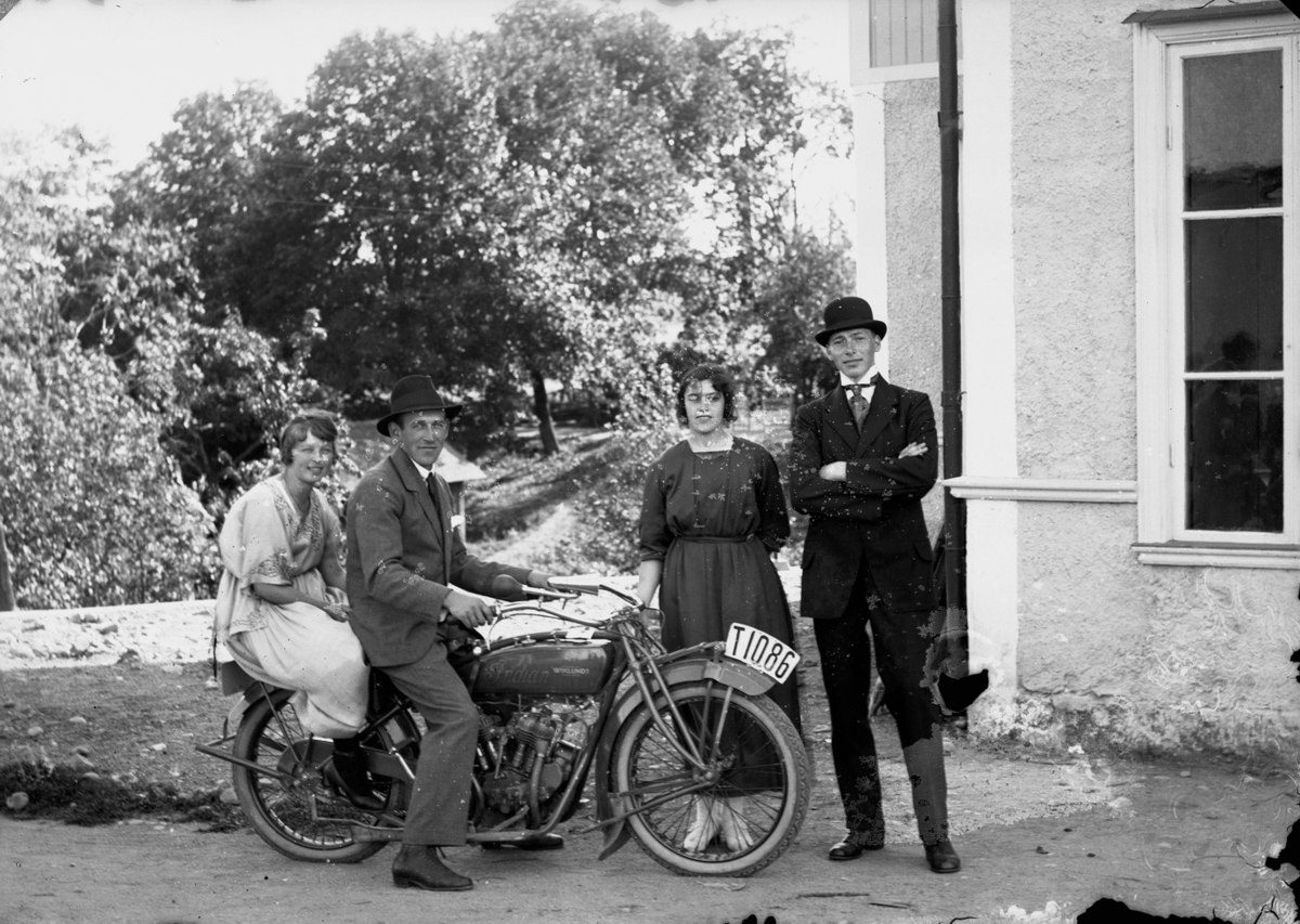 Fyra personer, två av dem på en motorcykel med registreringsnummer T1086, utanför Nya Norra Hyddan i Svennevad.
Stående: Anna Hallberg, född1896-03-13 vid Norra Hyddan i Svennevad och  Axel Hallberg, född 1899-05-16 vid Norra Hyddan i Svennevad. 
Motorcykeln är en Indian 5 hk som registrerades 28:e september 1920 och ägdes då av Gunnar Andersson, Örnsta, Hallsberg.