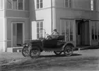 En man i en bil.
Bostadshus. 
Bilen är en Ford modell T Runabout från 1920-22.