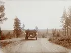 Vägen mellan Sunnemo och Filipstad. Herr Larsson går vid sidan om bilen. 
Bilen är en Oldsmobile modell 30 från 1923-24 med en 42 hästkrafters sexcylindrig motor. Den registrerades den 2:e april 1924 på fröken Jenny Larsson, Örebro, och fick registreringsnummer T99. År 1930 ägdes den fortfarande av Jenny Larsson.