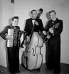 Swing-trio, tre män med musikinstrument (dragspel, bas och gitarr).
Sven Charlies Ensemble, Örebro. Fr. v. Sven Charlie Falk, dragspel och piano. Arne Olows, bas. Lasse Karlsson, gitarr och trumpet.