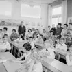 Rostaskolan, klassrumsinteriör, skolbarn med lärarinna. 
Sussis och Hasses examen.
Examen i andra klass,1961. Lärarinna Märta Ljung