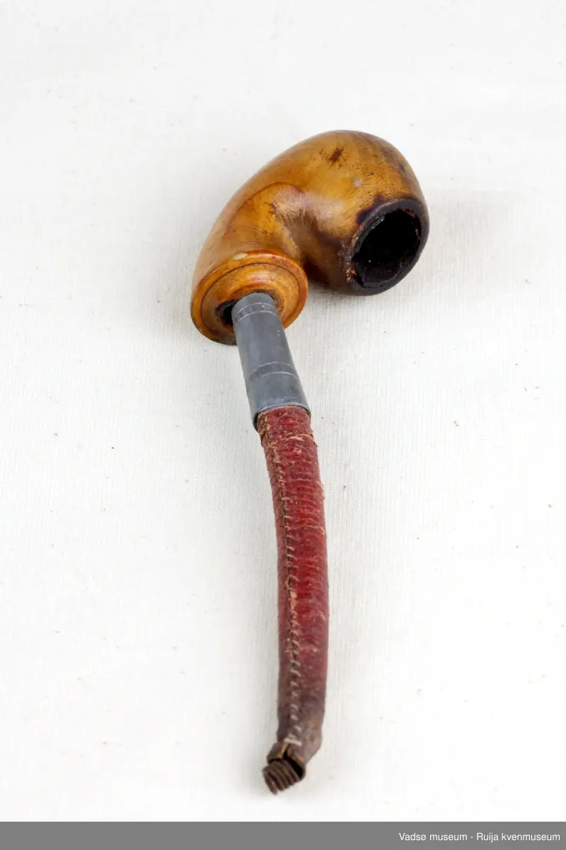 Pipe med liten hode av lyst tre. Skaftet av lær med spiral inni, ved overgangen til hodet kledt med tinn.
