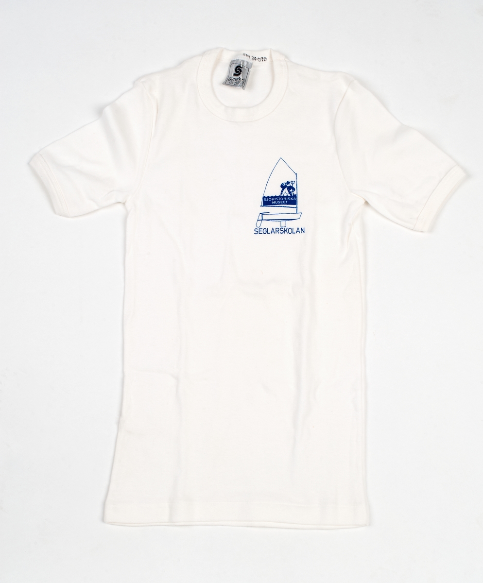 Vit t-shirt i barnstorlek 150. Tryck till vänster på bröstet: optimistjolle med sjökapten och treudd. "SJÖHISTORISKA MUSEET" i seglet samt SEGLARSKOLAN under skrovet.