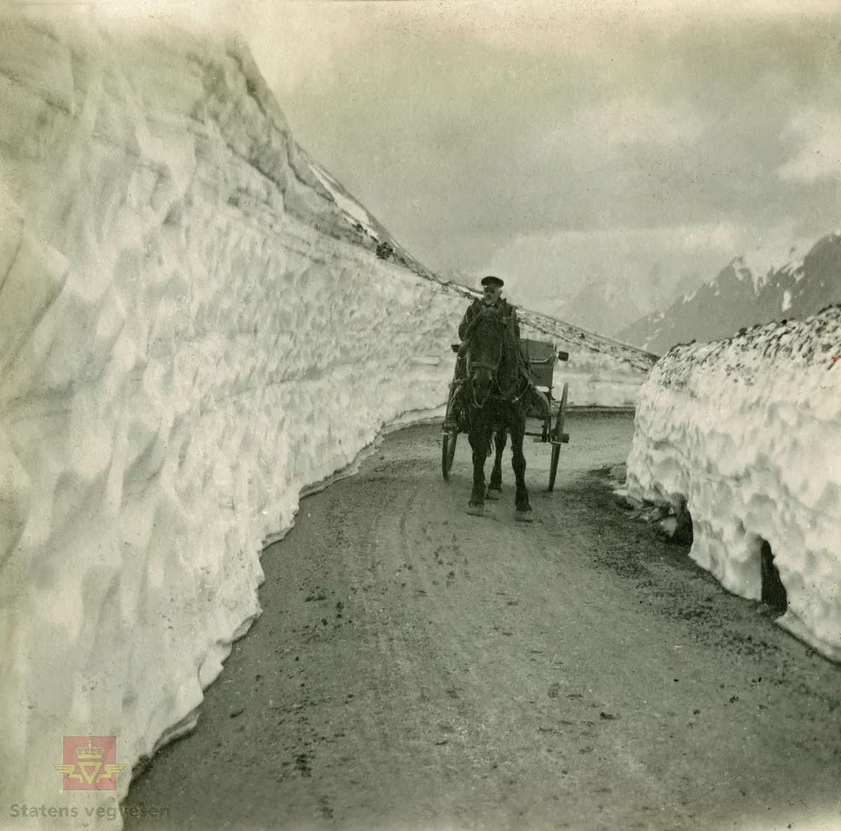 Album fra 1918-1934, "Snebrøyting." I følge merking: "Slyngen nedenfor Tystigen. Strynefjellsvegen 13. juli 1923."   Illustrasjonsbilder fra artikkel i  "Meddelelser fra Veidirektøren 1924, Nr. 43-54."   "Det Norske veivæsen 1274-1624-1824-1924." Side 165. Fig. 44. "Snemasser paa veien over Strynsfjeldet efter veiens farbargjørelse. Sogn og Fjordane fylke."