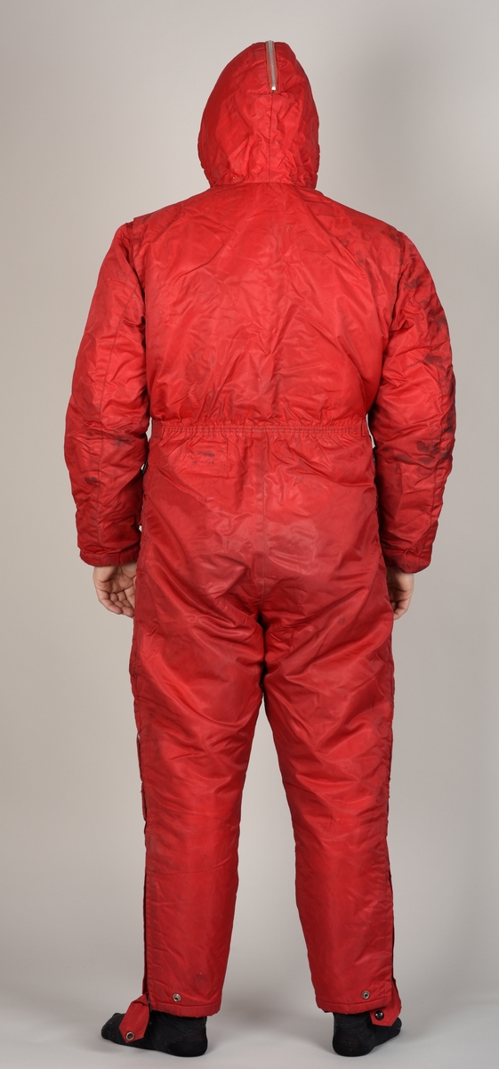 Rød dress med glidelås, hette, påsydd belte og to bukselommer.
Hetten har glidelås på oversiden.
Det er sydd på en sort stropp under hvert bein for å feste under skoene. Beltet lukkes med to halvrunde metallhemper.