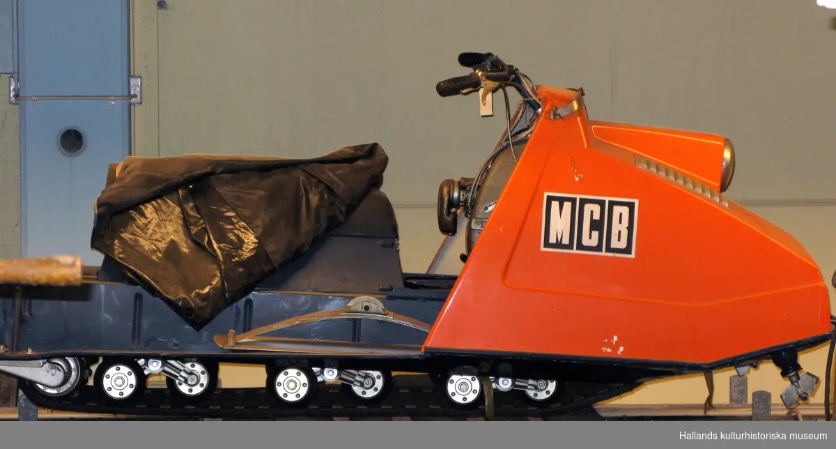 Snöskoter "MCB 520" (bandbredd 520 mm). Orange huv (front), blått chassi (bakparti). Bagageutrymme under sittdynan.
