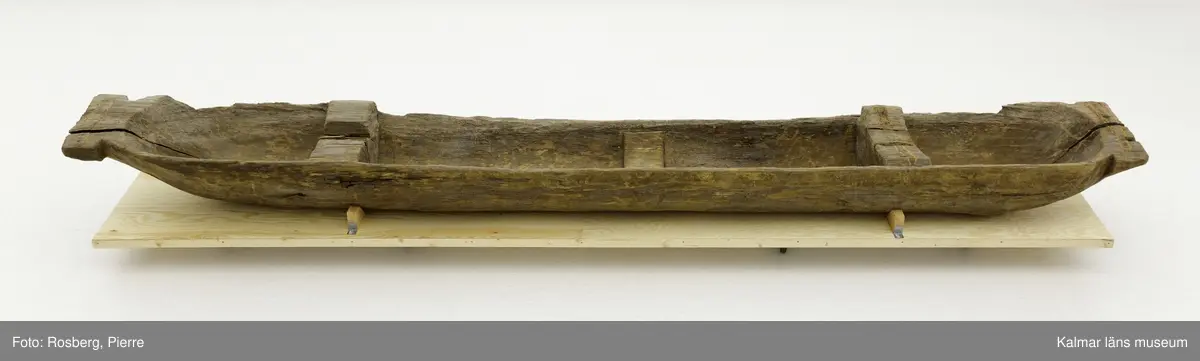 KLM 9352. Båt, stockbåt. Av stor urholkad trädstam, troligen furu. Huggen i ett stycke. Stamrunt tvärsnitt med runt, fallande överhäng. Två tofter och i mitten ett fotstöd. Går ej att uskilja för och akter. Rektangulära och rakt avskurna stävnockar, på den ena ett tamphål.