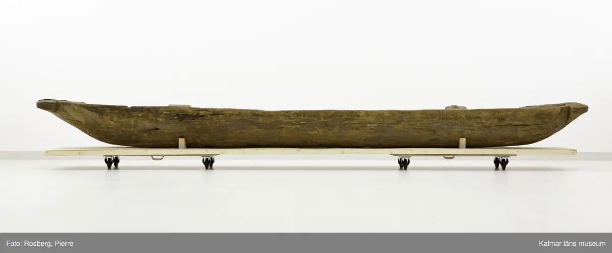 KLM 9352. Båt, stockbåt. Av stor urholkad trädstam, troligen furu. Huggen i ett stycke. Stamrunt tvärsnitt med runt, fallande överhäng. Två tofter och i mitten ett fotstöd. Går ej att uskilja för och akter. Rektangulära och rakt avskurna stävnockar, på den ena ett tamphål.