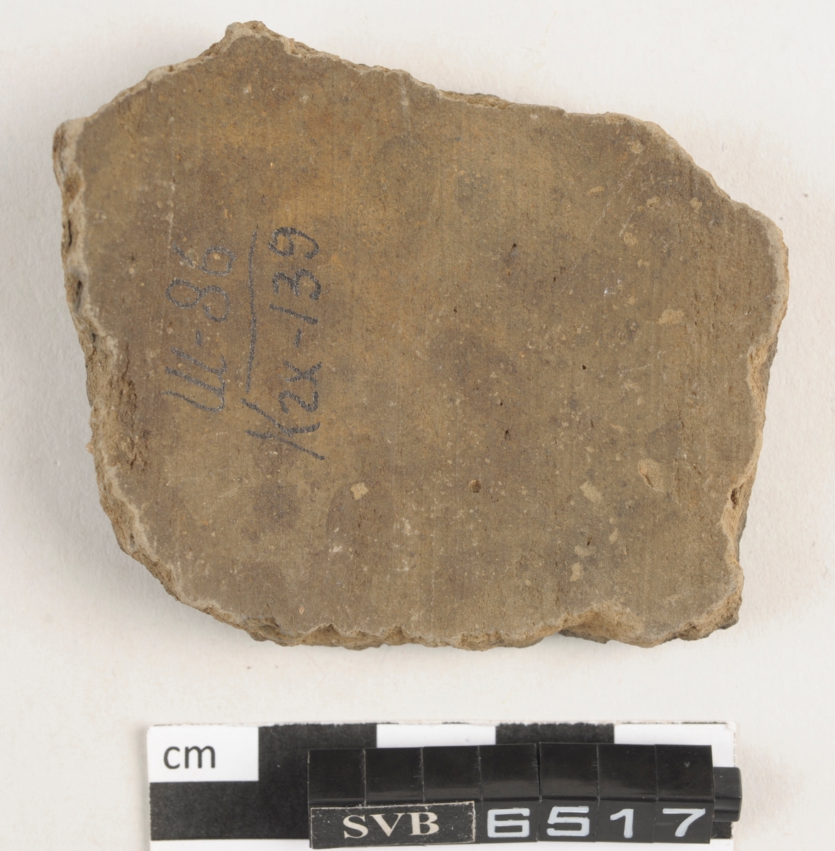 Buet keramikkfragment med bruddkanter. Fragmentet er brunt i farge.