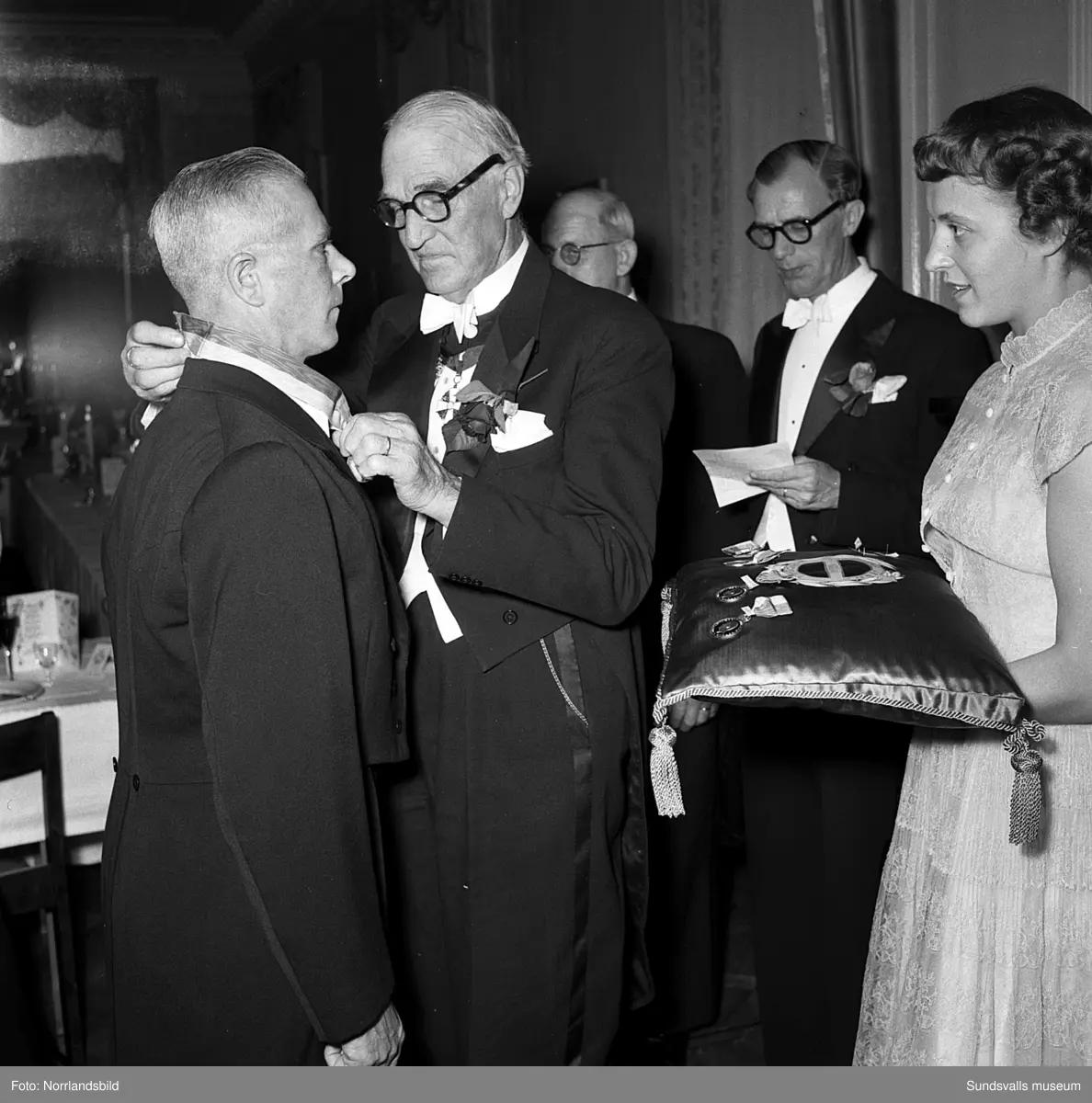 Ett urval av en stor grupp bilder från Lindgrens järnhandels 100-årsjubileumsfest på Knaust. Storstilad entré, mingel, utmärkelser, galamiddag och dans. Underhållning av bland annat en mycket ung Ingeborg Nyberg. På bilderna syns bland annat direktör Fridolf Brunnzell och lagerchefen Carl "Spiken" Lundberg, vilken samma år firade 50 år som anställd vid företaget.
