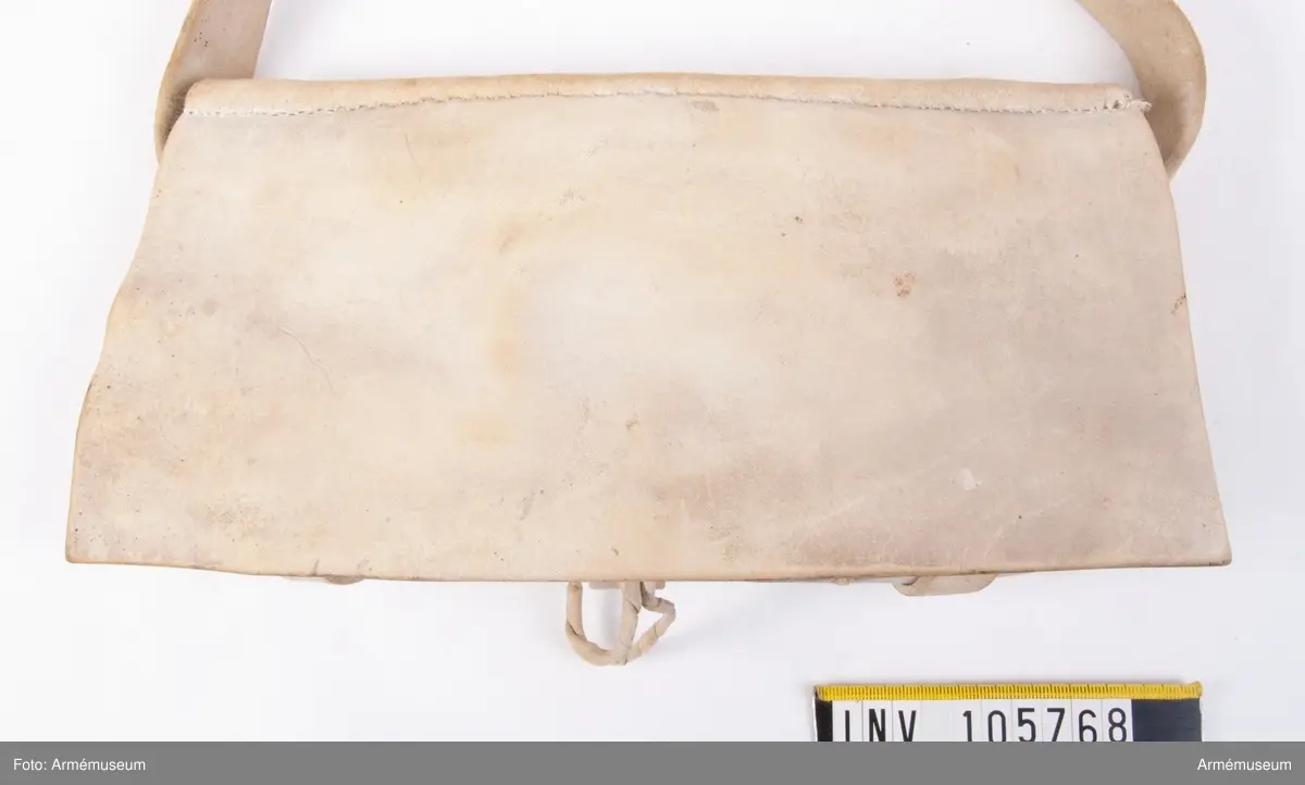 Patronväska av vitt sämskskinn med rem.
Inuti kartuchen finns en bleckplåtsinsats med rum för 12 patroner av ca 18 mm kaliber och plats för en liten oljeflaska. Under locket sitter även en extra ficka,
