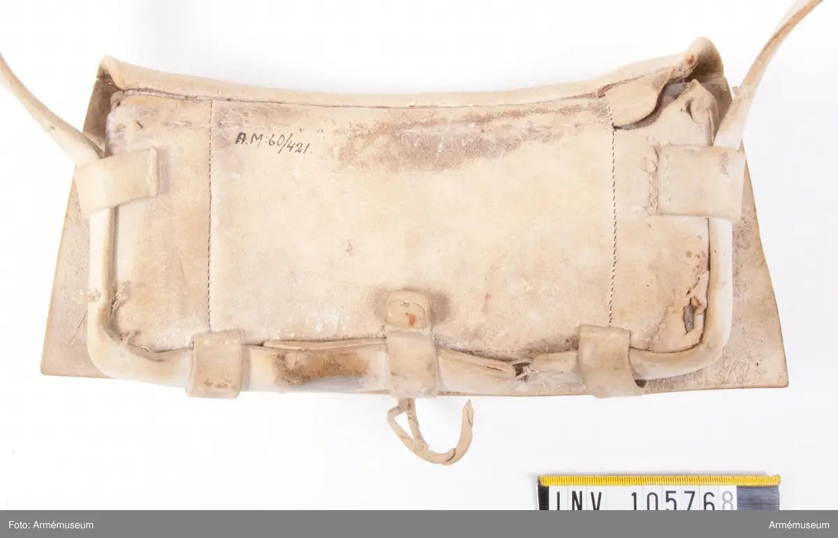 Patronväska av vitt sämskskinn med rem.
Inuti kartuchen finns en bleckplåtsinsats med rum för 12 patroner av ca 18 mm kaliber och plats för en liten oljeflaska. Under locket sitter även en extra ficka,