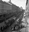 Förstamajtåget tågar i riktning söderut på Drottninggatan i Örebro den 1 maj 1937. Demonstrationståget består av många människor, varav några bär röda fanor, plakat och banderoller. På bägge sidor om gatan står åskådare och betraktar tillställningen. Som man kan se är detta förstamajtåg mycket långt.