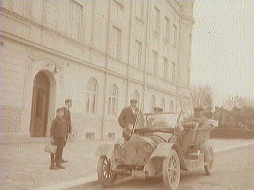 Män i bil utanför byggnad. 
Bilen på bilden är en 22 hästkrafters Mathis som ägdes av Gottfrid Thermaenius i Hallsberg. Den hade inregistrerats den 28:e april 1913 och hade registreringsnummer T123. År 1916 gjordes bilregistret om, och då fick bilen registreringsnummer T100. Gottfrid ägde bilen fram till 1921, då den såldes till Hallsbergs Elektricitetsverk. 1927 bytte den ägare igen och hade sedan fyra olika ägare under en kort period. Bilen skrotades slutligen i juni 1929.