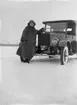 En kvinna vid en bil, registreringsnummer T18.
Hjälmaren den 17 februari. 
Bilen på bilden är en Gray Touring från 1922. Den ser ut att vara ny vid fototillfället eftersom den har en temporär registreringsskylt (interimsskylt).