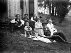 Familjegrupp sju personer i gröngräset. (Kaffedrickande).
Bilden är tagen på Almö-Lindö i Mälaren mellan Västerås och Lindö, ca 1918 då familjen gjorde en utflykt dit. Ön hörde till Fullerö herrgård. Det var en betesmark för djur. Där fanns då bara en gård som drevs av en man som hette Karlsson. Hans son gifte sig så småningom med Ulla (givarens kusin, dotter till hans morbror Evert).
Översta raden från vänster till höger:
OSKAR ERIKSSON, född 29/9 1885. Gift med givarens moster Elna, syster till hans mor Edit. Givaren berättar 