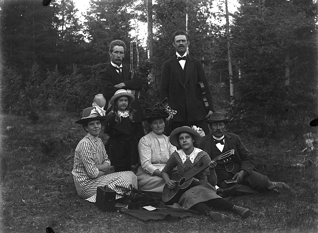 Grupp sju personer.
Till vänster familjen Edit och Johannes Natanael Bäckman med dottern Nanna och familjen Fält från Ullersäter med dottern Svea med gitarren.