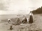 Fyra personer, och en hund, taxen Björn, på stranden. Båt i bakgrunden.
Doktorinnan Maria Norström, född Ekström, med sälskap.
Maria är gift med doktor Robert Norström, Örebro.
Hon är dotter till prosten/hovpredikanten Albert Ekström och Sofia 