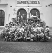 Samrealskola, gruppfoto, studenter.
Skolbyggnad i bakgrunden.