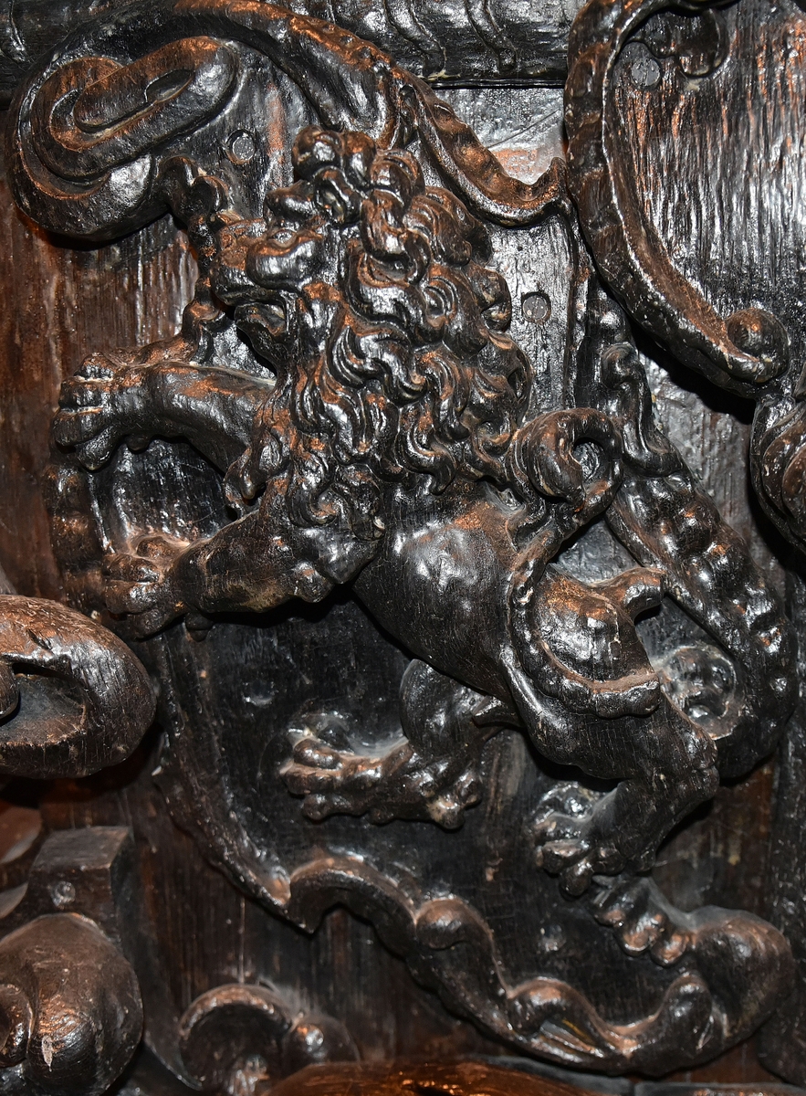 Skulpterad sköld, med upprätt, mot höger gående lejon. Lejonet är snidat i hög relief, med en heraldiskt stiliserad hållning. Sköldens kontur är rokokomässig, med kanter av varierande bredd och rik pärlbroskdekoration. Den vänstra kanten är något insvängd på mitten. Upptill avslutas skölden med en ellipsformad broskvolut. Baksidan är slät.

Text in English: Shield with upright, rightward-facing lion. The lion is carved in high relief and reproduced in perspective. It is seen in profile, and its posture is heraldically stylised. The shield has an almost rococo-like outline, with edges of varying width and rich earshell work decorations. The left-hand edge of the shield is somewhat narrowed at the middle.The top the shield is finished with an ellipse-shaped pearlwork scroll. The reverse side is smooth.