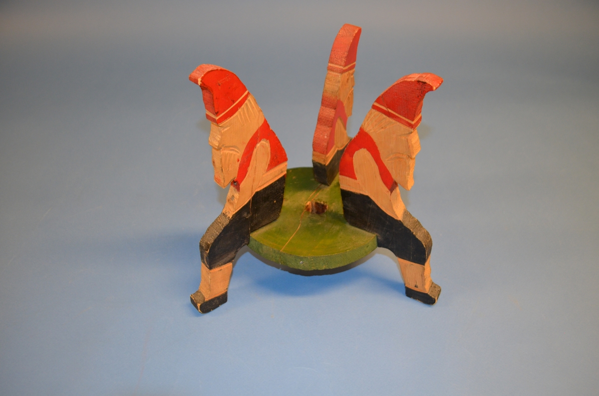 Hjemmelaget juletrefot av tre. Foten er satt sammen av tre støtter av hele trestykker formet som sittende nisser. I midten er et sirkelformet trestykke med hull for selve juletreet. Støtter og midtstykket er satt sammen med spiker. Juletrefoten er håndmalt. Nissene er malt i rødt og svart. Midtstykket grønt, med rosa underside.