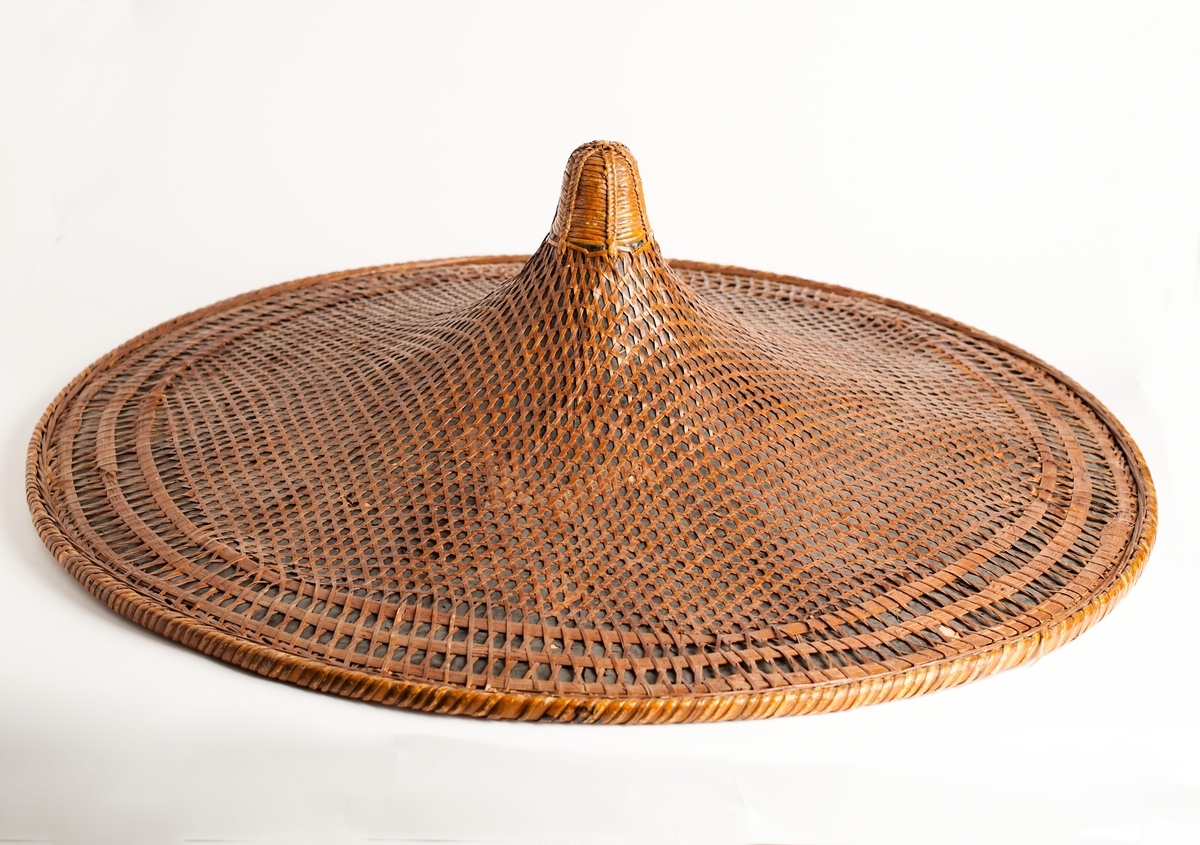Hatt från Kina av flätad bambufiber och palmblad, konisk, insvängd, bred bas. Stor men lätt.
Från fregatten Vanadis världsomsegling 1883-1885.