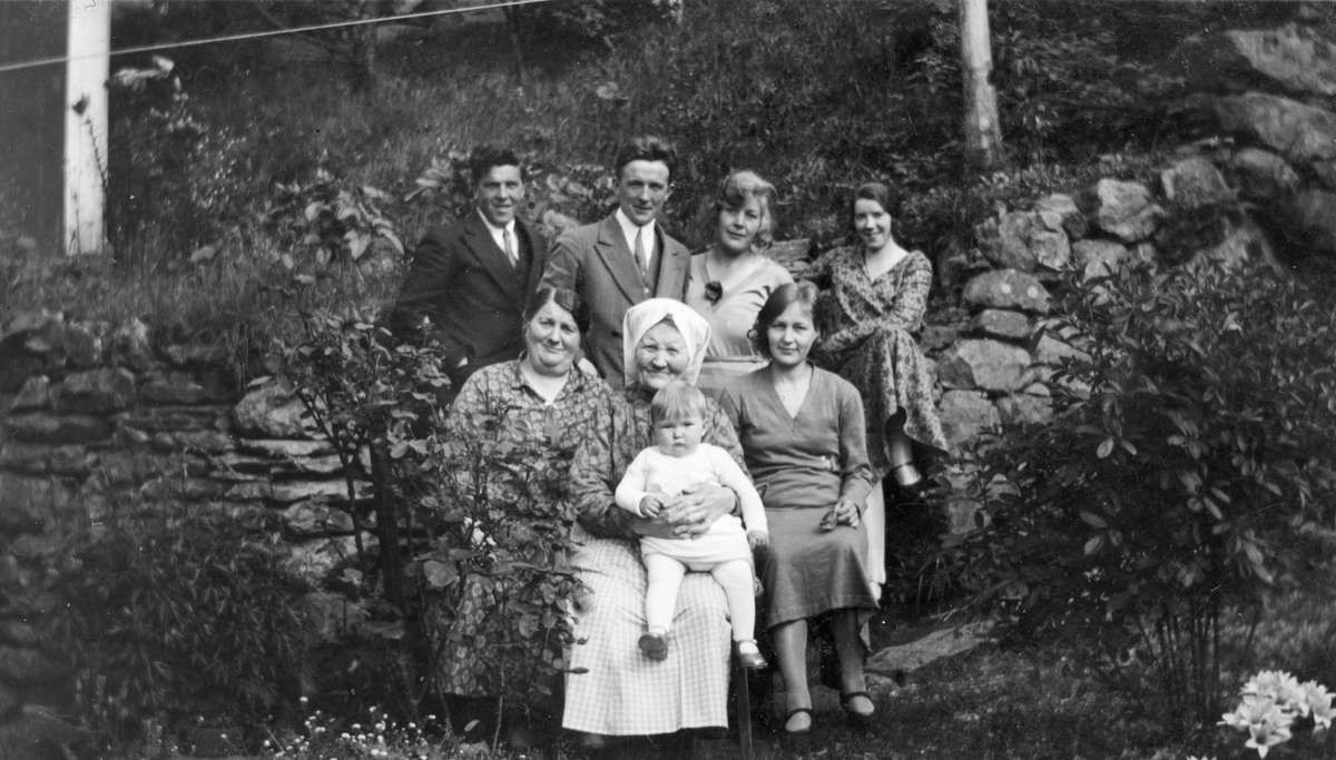 Familie i hagen utanfor Skåldalhuset, Salhus. 
Øvst frå venstre: NN, Knut Rasmussen Nordbø, NN, NN.
Nedst frå venstre: Karen Sofie Monsen Mjelde, Kari Mjelde med Åshild Rasmussen Nordbø på fanget.
