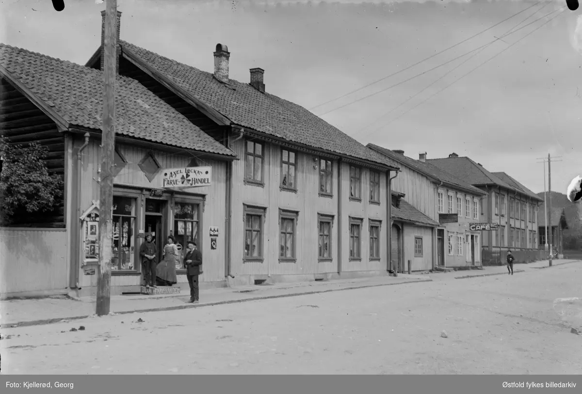 Storgata i Kongsberg. Nymoen skole øverst til venstre. 
Axel Løcka farvehandel. Cafe lenger nede i gata.
Iølge folketelling for 1910 i Kongsberg var det Axel Løkka f. 1887, handelsborger, og Antonette Arnesen handlende f. 1851 og Magna Olsen f. 1893, tjenestepike som bodde i huset.