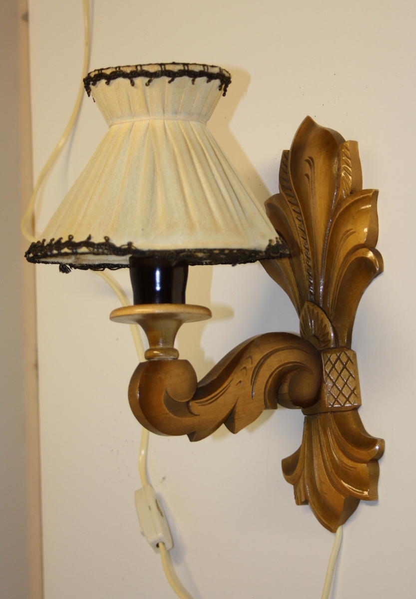 Vegglampe med fot i utskore tre og skjerm med tekstiltrekk.