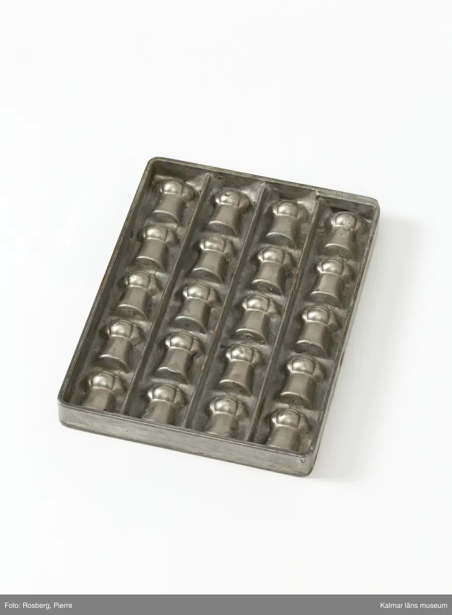 KLM45785:1. Form. Av tenn. Gjutform för chokladpraliner. Formen för pralinerna förefaller vara en champagnekork. 20 praliner finns det plats för att gjuta i formen. På ena långsidan text, Anton Reiche Dresden Nacn No 16640.