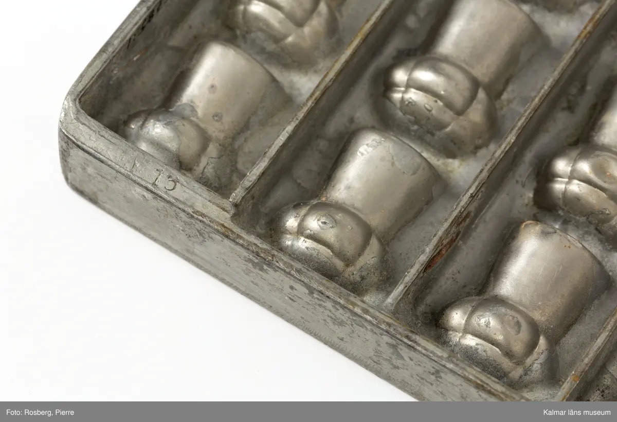 KLM45785:1. Form. Av tenn. Gjutform för chokladpraliner. Formen för pralinerna förefaller vara en champagnekork. 20 praliner finns det plats för att gjuta i formen. På ena långsidan text, Anton Reiche Dresden Nacn No 16640.