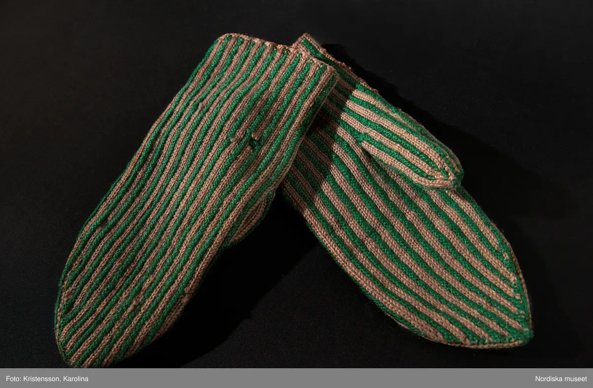 Ett par kvinnovantar stickade av ullgarn, smalrandiga i grönt och ljusbrunt. De ljusbruna ränderna består av 2 maskor slätstickning och de gröna av 2 aviga  maskor,  där de 2 färgerna  hela tiden följer med  och flotterar på avigsidan. Det ger en stum yta utan elasticitet. 
Anm Den högra vanten mer sliten med flera stoppningar med det gröna garnet.
Har tillhört Augusta Davidsson, "Snögges Augusta" f. 1868 i Habo död 1950 på ålderdomshemmet. Hon hade bott hela sitt liv i föräldrahemmet ett soldattorp under Vagnhult i Habo. hennes far var soldat liksom brodern Efraim. Först vårdade hon modern i hemmet, senare hushållade hon åt den ogifte brodern Efraim. Sen gick hon på "hjälpe" hos bönderna i bygden. Foto av stugan skall finnas i museet. Kläderna som museet mottagit är de som hon hade med sig till ålderdomshemmet.
/Berit Eldvik 2013-03-11