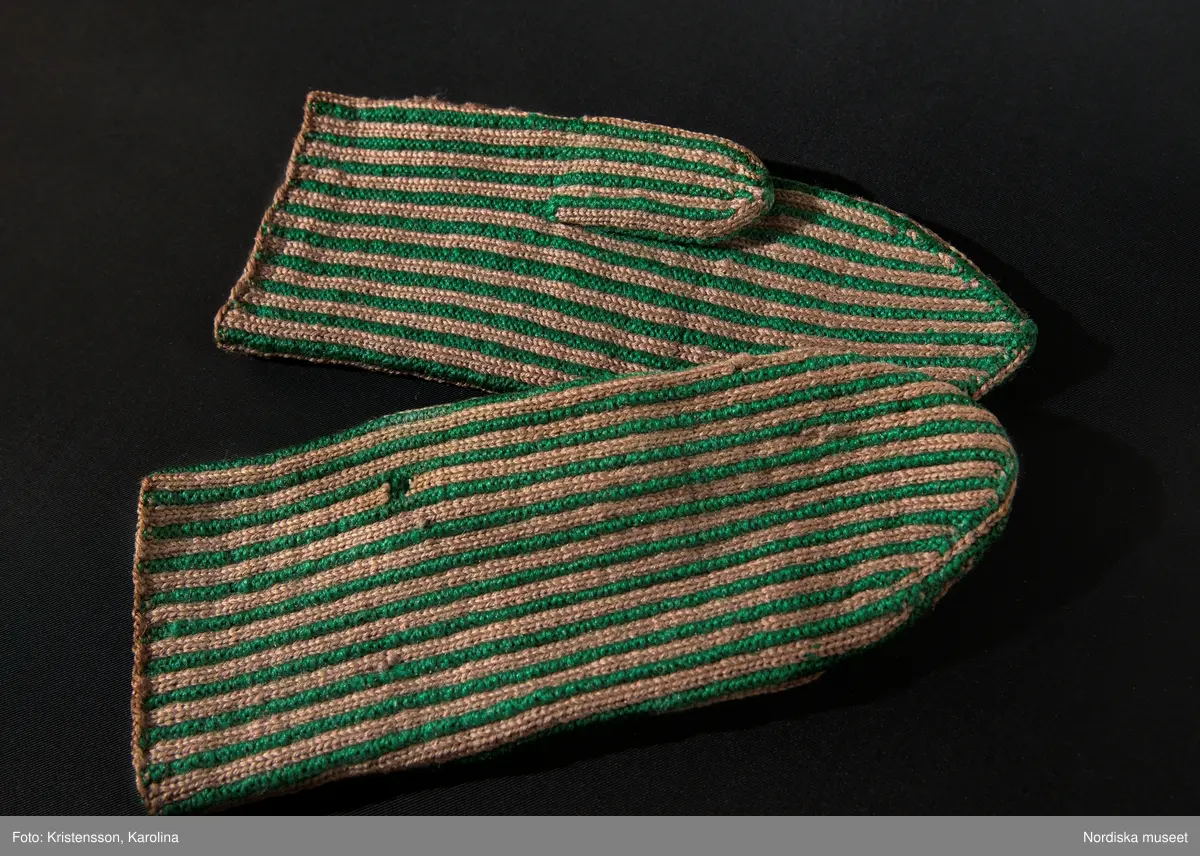 Ett par kvinnovantar stickade av ullgarn, smalrandiga i grönt och ljusbrunt. De ljusbruna ränderna består av 2 maskor slätstickning och de gröna av 2 aviga  maskor,  där de 2 färgerna  hela tiden följer med  och flotterar på avigsidan. Det ger en stum yta utan elasticitet. 
Anm Den högra vanten mer sliten med flera stoppningar med det gröna garnet.
Har tillhört Augusta Davidsson, "Snögges Augusta" f. 1868 i Habo död 1950 på ålderdomshemmet. Hon hade bott hela sitt liv i föräldrahemmet ett soldattorp under Vagnhult i Habo. hennes far var soldat liksom brodern Efraim. Först vårdade hon modern i hemmet, senare hushållade hon åt den ogifte brodern Efraim. Sen gick hon på "hjälpe" hos bönderna i bygden. Foto av stugan skall finnas i museet. Kläderna som museet mottagit är de som hon hade med sig till ålderdomshemmet.
/Berit Eldvik 2013-03-11