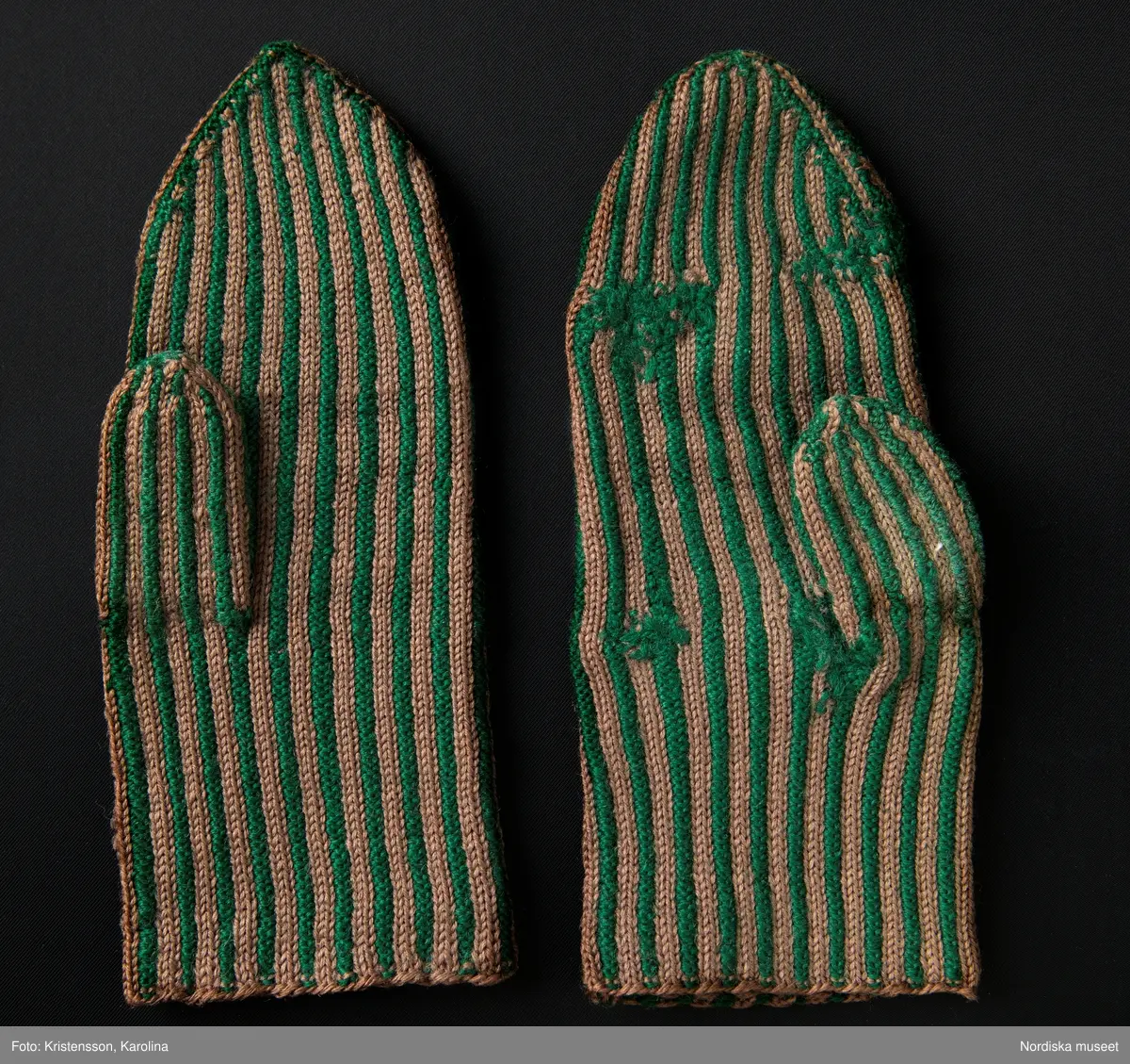Ett par kvinnovantar stickade av ullgarn, smalrandiga i grönt och ljusbrunt. De ljusbruna ränderna består av 2 maskor slätstickning och de gröna av 2 aviga  maskor,  där de 2 färgerna  hela tiden följer med  och flotterar på avigsidan. Det ger en stum yta utan elasticitet. 
Anm Den högra vanten mer sliten med flera stoppningar med det gröna garnet.
Har tillhört Augusta Davidsson, "Snögges Augusta" f. 1868 i Habo död 1950 på ålderdomshemmet. Hon hade bott hela sitt liv i föräldrahemmet ett soldattorp under Vagnhult i Habo. hennes far var soldat liksom brodern Efraim. Först vårdade hon modern i hemmet, senare hushållade hon åt den ogifte brodern Efraim. Sen gick hon på "hjälpe" hos bönderna i bygden. Foto av stugan skall finnas i museet. Kläderna som museet mottagit är de som hon hade med sig till ålderdomshemmet.
/Berit Eldvik 2013-03-11