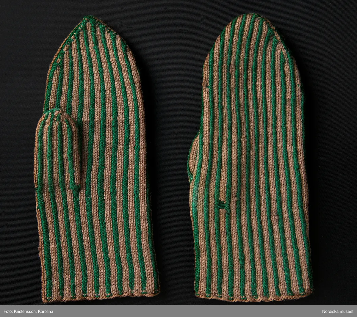 Ett par kvinnovantar stickade av ullgarn, smalrandiga i grönt och ljusbrunt. De ljusbruna ränderna består av 2 maskor slätstickning och de gröna av 2 aviga  maskor,  där de 2 färgerna  hela tiden följer med  och flotterar på avigsidan. Det ger en stum yta utan elasticitet. 
Anm Den högra vanten mer sliten med flera stoppningar med det gröna garnet.
Har tillhört Augusta Davidsson, "Snögges Augusta" f. 1868 i Habo död 1950 på ålderdomshemmet. Hon hade bott hela sitt liv i föräldrahemmet ett soldattorp under Vagnhult i Habo. hennes far var soldat liksom brodern Efraim. Först vårdade hon modern i hemmet, senare hushållade hon åt den ogifte brodern Efraim. Sen gick hon på "hjälpe" hos bönderna i bygden. Foto av stugan skall finnas i museet. Kläderna som museet mottagit är de som hon hade med sig till ålderdomshemmet.
/Berit Eldvik 2013-03-11
