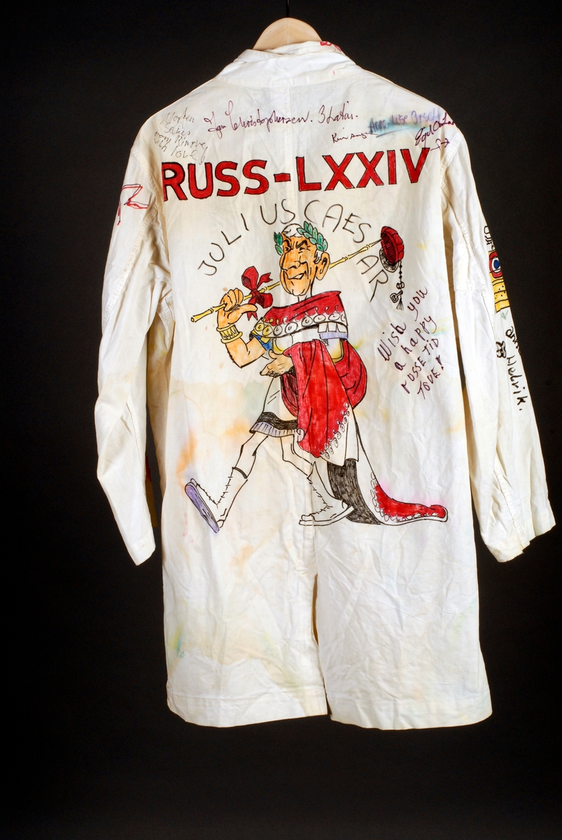 Russefrakk med slag, lommer og knapper. På baksiden er det et bilde av Julius Caesar med rød russelue og russestokk. Over står det skrevet RUSS - LXXIV (74). På høyre lomme er det et bilde av Hårek, mens det på venstre lomme er et bilde av Kark. Opp av brystlommen vokser det en rød blomst. På høyre bryst er det tegning av et rødt eåle og en strektegning av en sort og hvit katt. Det er en del navnetrekk på frakken, men ellers lite tekst.
Det følger også med en rød russelue med navnetrekk på. I dusken er det festet en champagnekork. Det er også knuter i dusken.