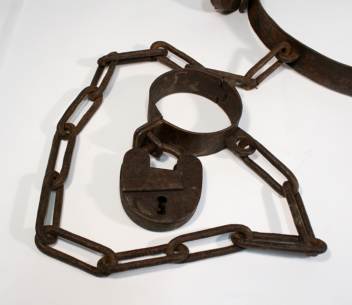 Hals, liv og fotjern festet sammen med lenke. Alle har en hengelås festet.