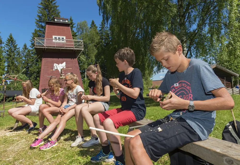 Bildet viser en gruppe elever som sitter å spikker. Det er sommer.