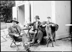 Fotografi av tre herrar samt en hund, vid cafébord.