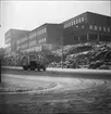 Ljusbild, fotografi av väg invid större bygnad, fabriksbyggnad, skola?