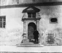 Skioptikonbild med motiv av man på trappa, betraktande port, Rothenburg.
Bilden har förvarats i kartong märkt: Rothenburg VI. 1901. 5