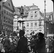 Skioptikonbild med motiv av folkvimmel kring Augustbrunnen, fontän i Augsburg.
Bilden har förvarats i kartong märkt: Augsburg 1901. 13. Text på bild: 