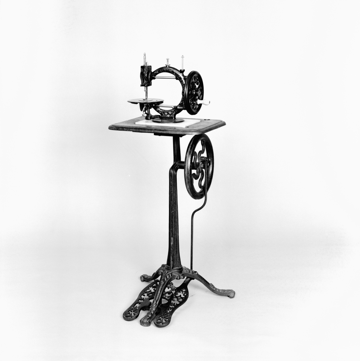 Handdriven symaskin på marmorplatta."The little Wanzer", för dubbeltrådig söm, med fram- och återgående skyttel enligt Howes patent. Märkt: R.M. Wanzer & Co. Patentees & Manufs Hamilton Canada West: Time utilizer. Trade (timglas) mark. Patented in America Gt Britain and the continent May 16 & June 17 1867".
Tillbehör: låda av trä med skjutlock och handtag, trälådans mått: 360x310x185,  Vikt:3,3kg, starkt sliten,  skyttel, 5 st spolar (2 saknas), 4 st fållvikare (saknas), 2 st ramar (?) för brodering(?), 2 st hållare (?) för brodering (?), 2 st kulor med filt (smörjkoppar ?).