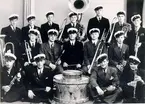 Mössebergs musikkår 1940. Övre raden: Evert Moberg, Arnold Ewertz, Rune Olofsson, Lennart Lind, Oskar Nilsson, Axel Josefsson, Åke Dahlin. Mitten: Olle Carlsson, Arvid Pompeijus, Henrik Larsson, John Gustafsson, Arne Johansson. Nedre raden: Stig Johansson (han bytte namn till Sennerfors), Nils Milen, Stig Eriksson, Karl-Erik Roos.