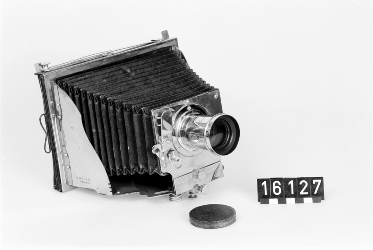 This was the first metal folding camera, the Model II. It was designed with a patent by H. Mader in 1888-1890. The camera was donated to the museum in January 1939 by Helmer Bäckström, who was a professor of photography. The camera is marked "5" in the slats of the bellows as well as with a round mark with the letters G M R and two sword-like characters. The lens is marked "Aplanal Invincible" and has "VI" engraved on the back at the threads. The camera comes with four cassettes, five plug-in apertures and a textile-clad case.