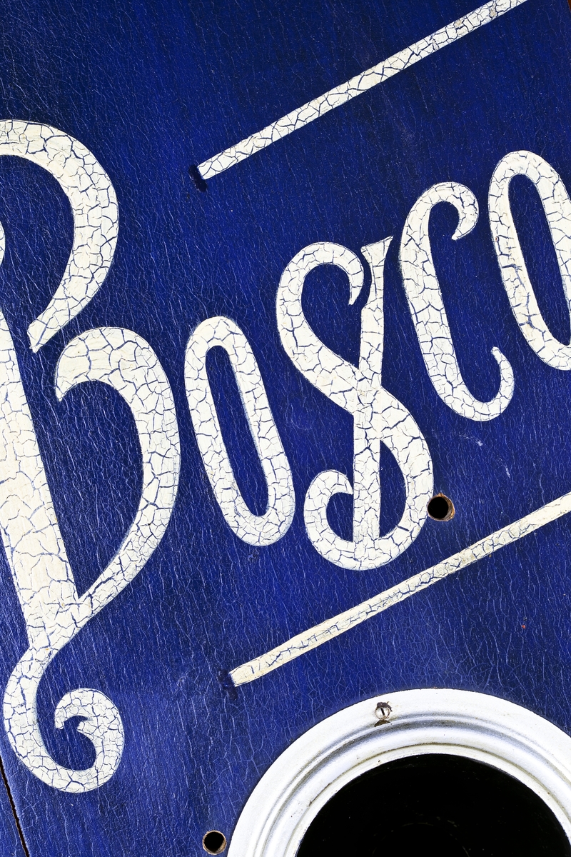 Fotoautomat "Bosco" för tillverkning av ferrotypier. Penningautomat för självfotografering.  Den fungerade på så sätt att det ljuskänsliga skiktet placerats i en profilerad plåtbricka som på samma gång var framkallningsskål och sedan ram för fotografiet. I automaten exponerades bilden i lodrätt läge och framkallades sedan med vätskor som portionerades ur behållare. Efter tre minuter var ferrotypen klar och matades ut ur apparaten. Den behövde torka ytterligare och fick enligt anvisningarna inte utsättas för starkt ljus förrän den var torr. Bilden mätte 60x83 mm och levererades i ett etui av papper. Plåtbrickan hade påtryck av reklam och information på baksida och kanter.
Tillbehör: Sockel med 2 st. metallådor för plåtar, 10 st. plåtar ("W.H.C Bernitt Original Bosco Platte Hamburg 23 ...), överdel med kamera, mekanism, mekanism för framkallning m.m. nyckel till verket.