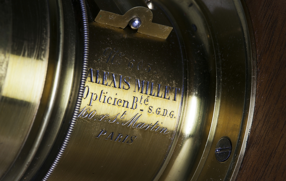 Kamera, skjutlådemodell. Våtplåt 9,5 x 11,5. Objektiv: Alexis Millet, Opticien Bte'SGDG 160r.st:Martin Paris. Nr 605. Utrustning för fotografering på resor, jämte koffert. Lösa delar: kamera av trä med objektiv från Alexis Millet, Paris, nr. 605, objektivlock av mässing, visirskiva, 4 kassetter för våtplåtar 9 x 12 cm, bakstycke med visirskiva för stereobilder 8 x 8 cm, 2 kassetter för stereovåtplåtar, kärl av zinkplåt med lock (gångjärnet avbrutet), trattformat kärl av zinkplåt, mindre kuvert av glas (spräckt och lagad, troligen av givaren), större kuvert av glas, torkställ av trä, 2 skivor av trä med spår för plåtar, kopieram för max 16 x 20 cm, vikbar skiva av trä (för beredning, troligen av våtplåtar), liten bordskiva med kantlist (passar till stativet TM 25.111,fodral av trä med 12 st. våtplåtnegativ 9 x 12 cm (porträtt och skulpturer), fodral av trä med 12 st. sämre negativ, fodral av trä med 10 st. blanka och  skrapade glasplåtar, diverse plåtar i paket (i ask ny 1950), fodral av trä med 11 st. stereovåtplåtar, varav 3 preparerade.
Tillbehör: Koffert.